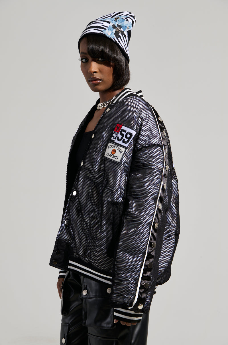 A person wearing a black and white knit beanie stands against a plain background, layered under the PLAYERS ONLY Jersey Bomber, which features a shiny, textured finish and athletic patches. Matching black leather pants complete the look.