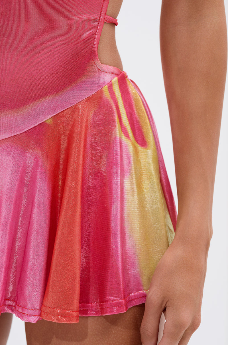 A close-up of a person wearing the YOU WISH PRINTED MINI DRESS, featuring a vibrant abstract pattern, flared skirt, and thin straps, highlighting their side and arm against a plain background.