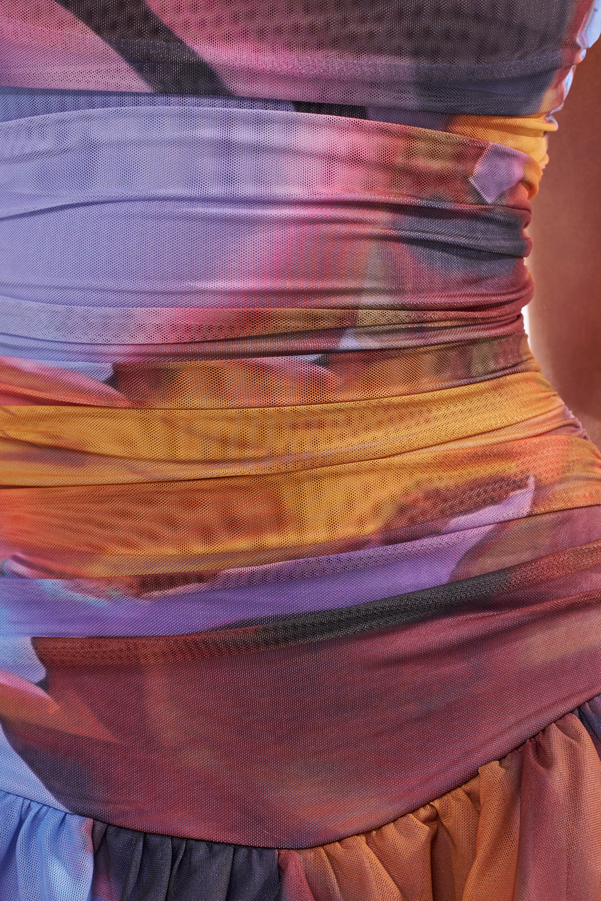 Close-up of the IN A MOOD PRINTED MINI DRESS IN PURPLE, a tie-dye mini dress in purple, orange, yellow, and red with ruched detailing and soft pleats at the waist and hips. 9
