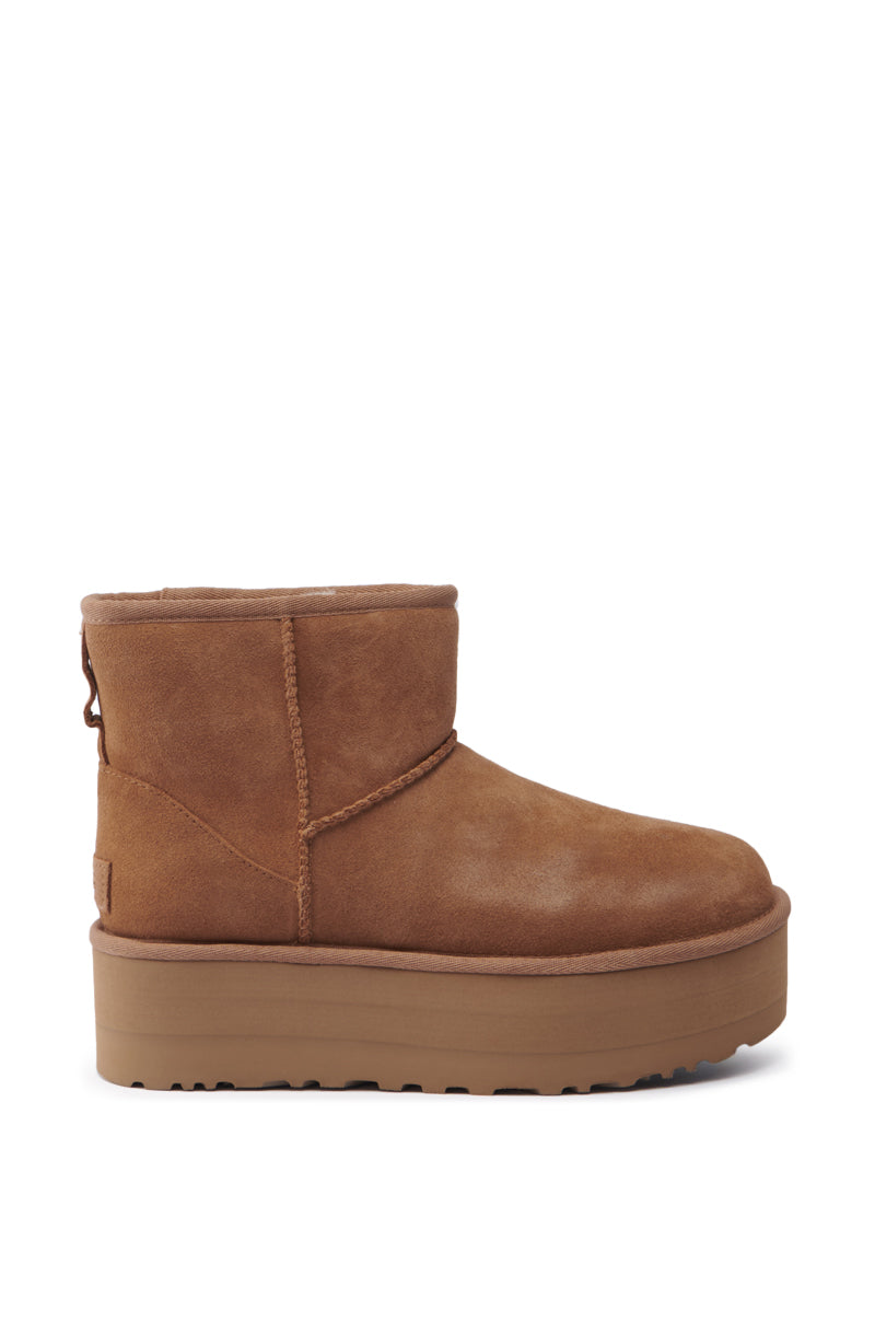 A single UGG Classic Mini Platform Bootie in Chestnut, featuring an ankle-height shaft and chunky sole, is displayed against a plain white background. The brown suede boot showcases a visible seam running along its side, adding both style and structure.