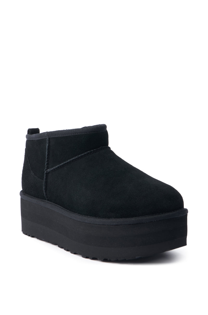 Introducing the UGG Classic Ultra Mini Platform in Black, a chic ankle boot featuring a minimalist design with a thick sole. This suede platform bootie comes with a rounded toe and an easy pull tab at the back, crafted for ultimate comfort and effortless style elevation.