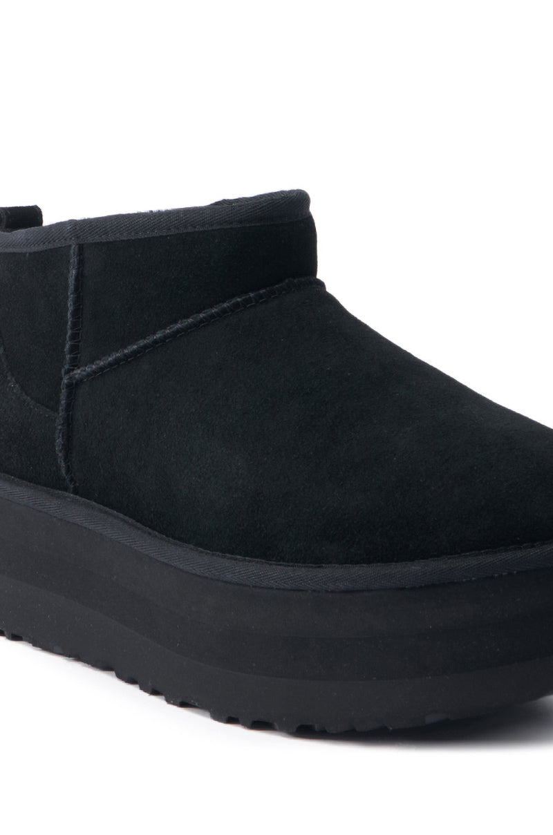 A close-up view of the UGG Classic Ultra Mini Platform in Black showcases its suede material and thick rubber soles with visible stitching. This stylish bootie features a minimalist design with a round toe, inspired by the iconic UGG Classic Ultra Mini, ensuring both style and comfort.
