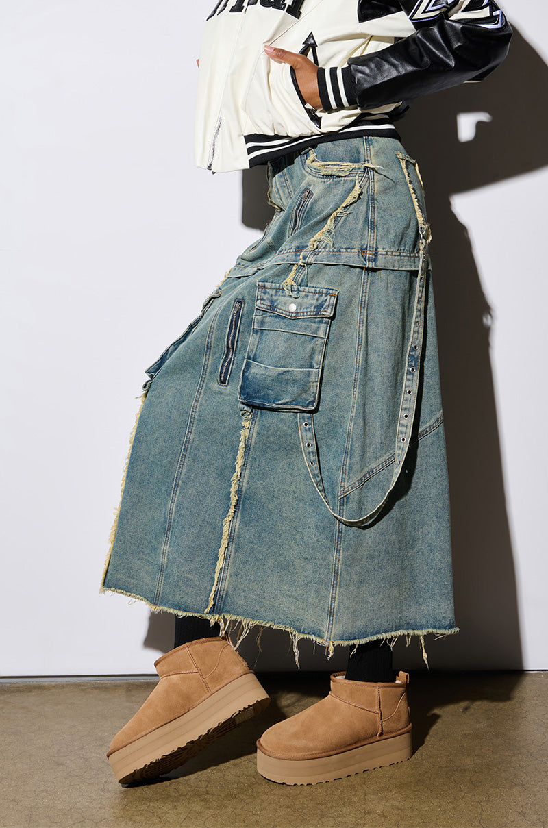 The image features a person wearing a long, distressed denim skirt with multiple pockets, paired with a white jacket. They are also sporting the UGG Classic Ultra Mini Platform in Chestnut. The photo focuses on the lower half of the body against a plain background, emphasizing the fashion-forward style featuring a wool blend upper.
