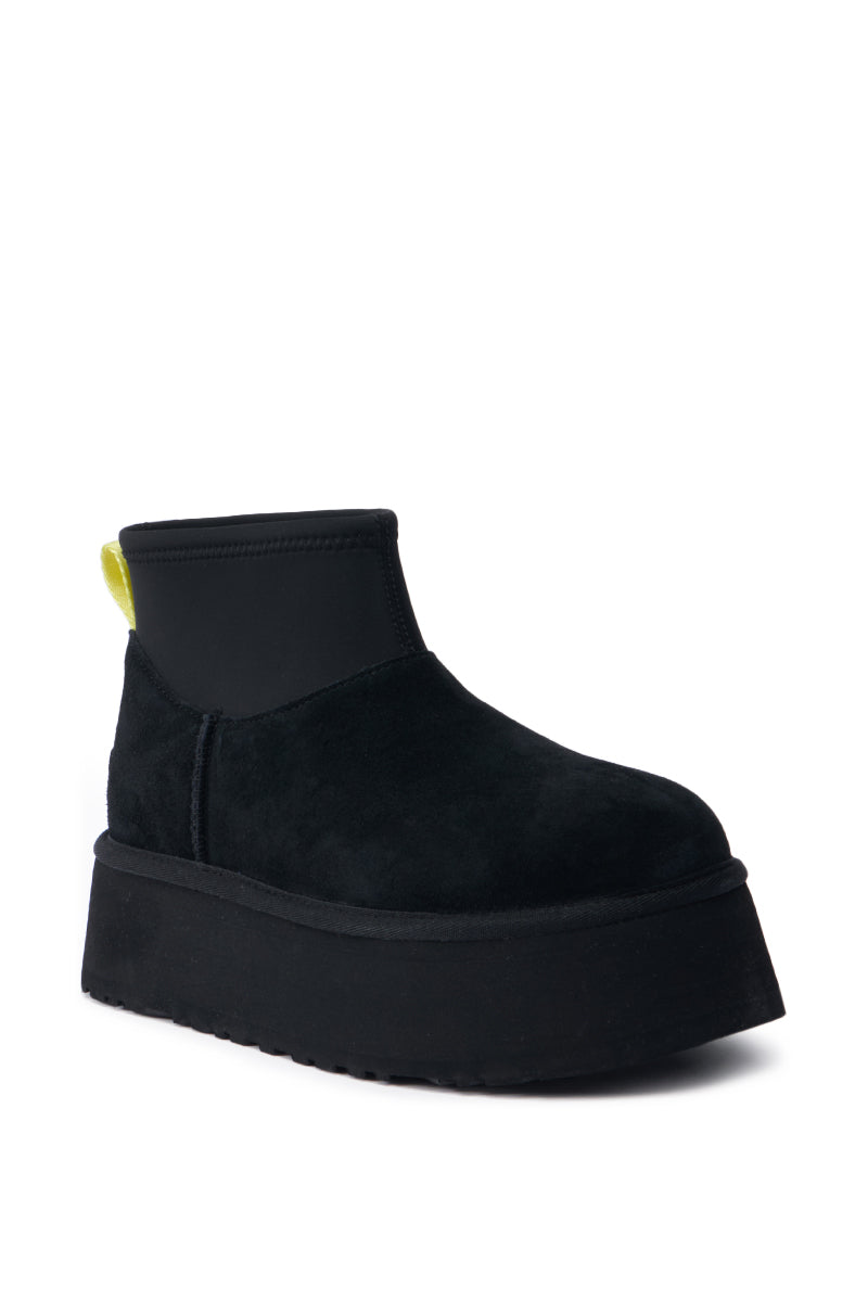 Introducing the UGG CLASSIC MINI DIPPER IN BLACK: This ankle-high platform shoe showcases a plush suede upper complemented by a striking neon yellow pull tab at the back. Its sleek, minimalist design effortlessly embodies modern style.