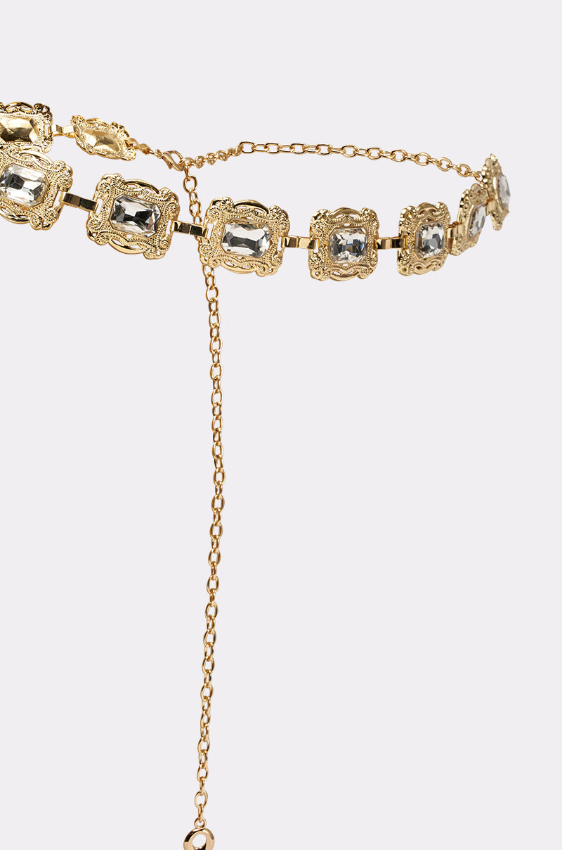 The GODDESS VIBES CHAIN BELT is a vintage glam accessory with ornate square settings, clear gemstones, gold links, and a dangling chain with clasp, showcased on a plain light background. 3