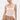A woman with slicked-back hair models the NEW STANDARD SQUARE NECK SLEEVELESS BODYSUIT IN BEIGE, paired with a tan skirt and gold accessories. She stands against a plain white background, gazing slightly to the side.