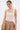 A woman with slicked-back hair models the NEW STANDARD SQUARE NECK SLEEVELESS BODYSUIT IN BEIGE, paired with a tan skirt and gold accessories. She stands against a plain white background, gazing slightly to the side.
