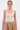 A woman with slicked-back hair wears the NEW STANDARD SQUARE NECK SLEEVELESS BODYSUIT IN BEIGE, styled with a tan buttoned skirt, gold hoop earrings, and a gold arm cuff, standing against a white background.