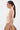 A woman with long straight brown hair in a low ponytail wears the NEW STANDARD SQUARE NECK SLEEVELESS BODYSUIT IN BEIGE, a tan skirt, gold hoop earrings, and three gold arm cuffs, standing in profile against a plain white background.