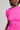 In a vibrant CAMARI RUCHED MIDI DRESS, a woman radiates elegance with its bright pink, off-the-shoulder design. Her face is partially visible, decorated with colorful dangling earrings, and the plain light-colored background perfectly accentuates the vividness of her ensemble.