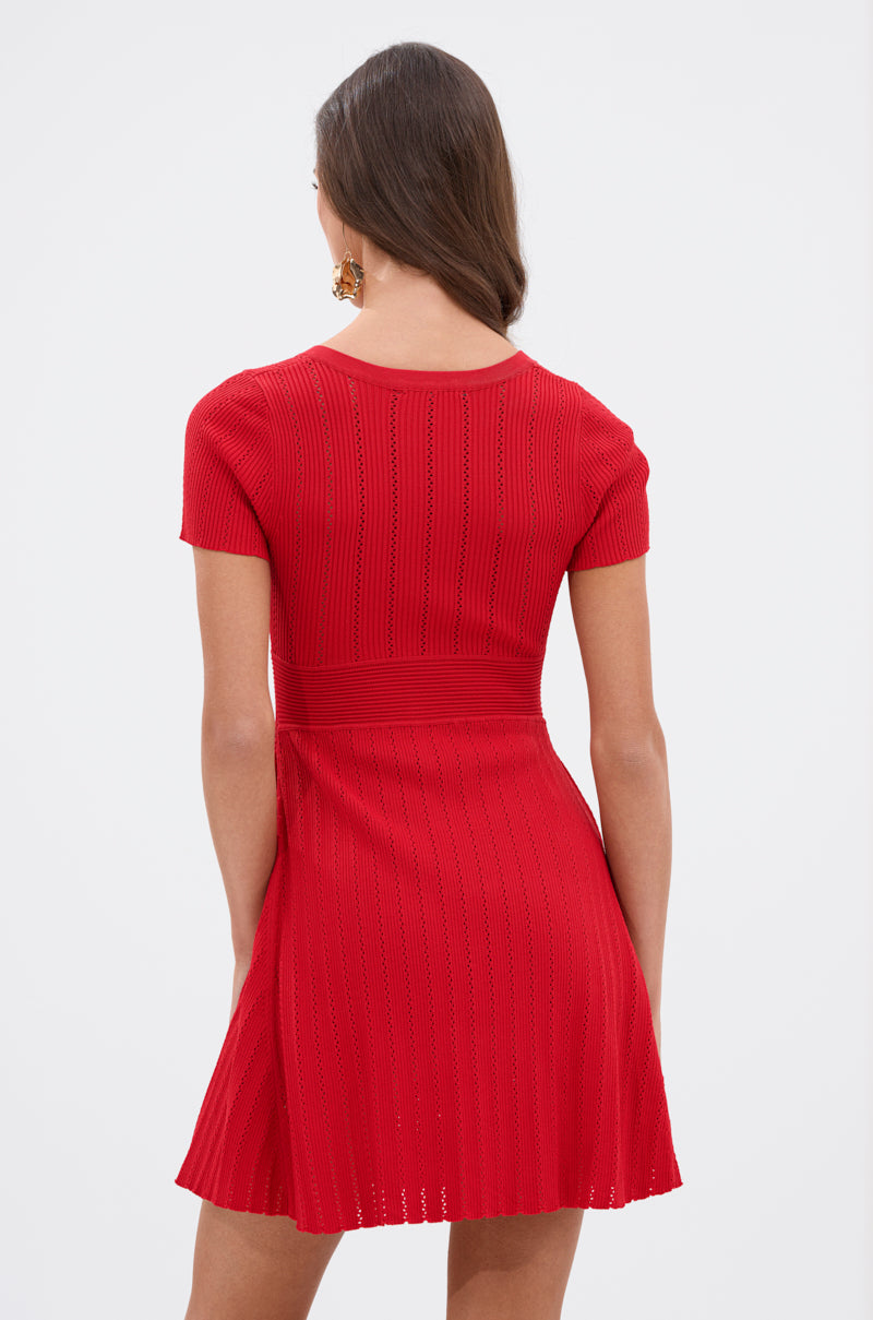A woman with long brown hair is shown from the back against a plain light background, wearing the RUBY RED MINI DRESS, a textured ribbed knit mini dress featuring short sleeves. 3