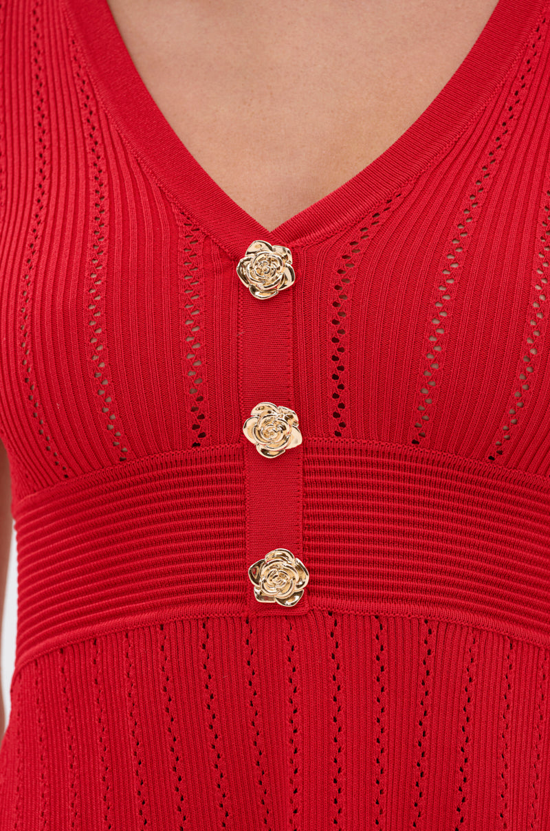 Close-up of the RUBY RED MINI DRESS with a V-neckline, ribbed knit texture, three gold floral buttons, intricate vertical patterns, delicate openwork details, and an A-line hem. 6