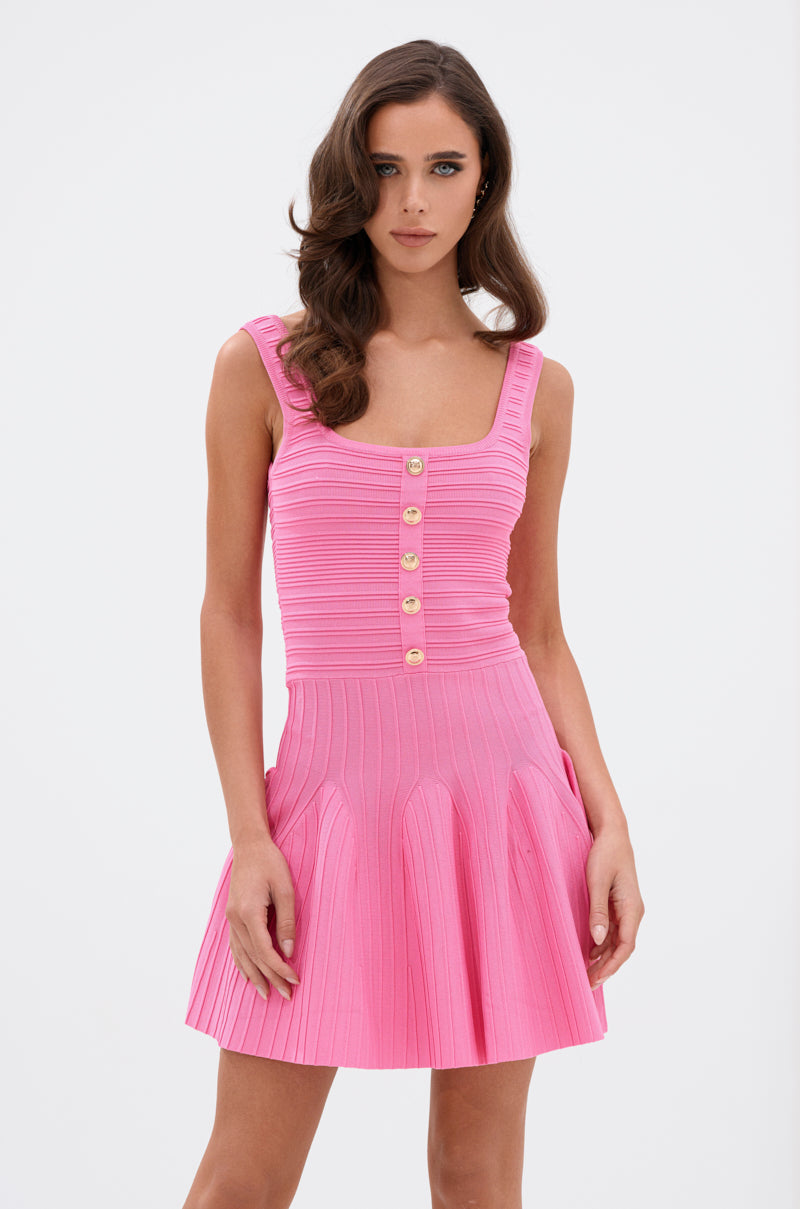 A woman with wavy brown hair wears the ROSE MINI DRESS, featuring a sculpted bodice, button-down front, and flared ribbed knit skirt, standing against a plain white background.