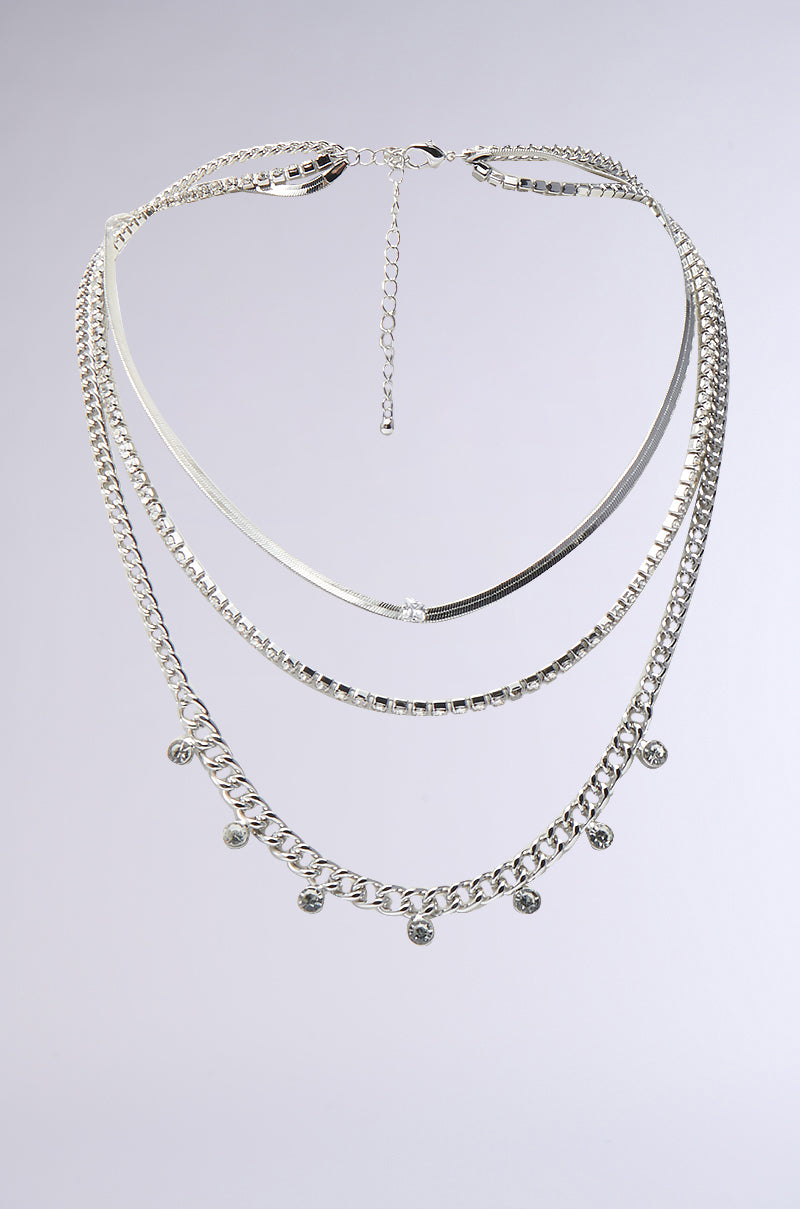 The LAYERED UP SILVER NECKLACE features a snake chain, a curb chain with round charms, and a simple curb chain joined by one clasp and extender, shown on a neutral background for versatile silver styling. 0