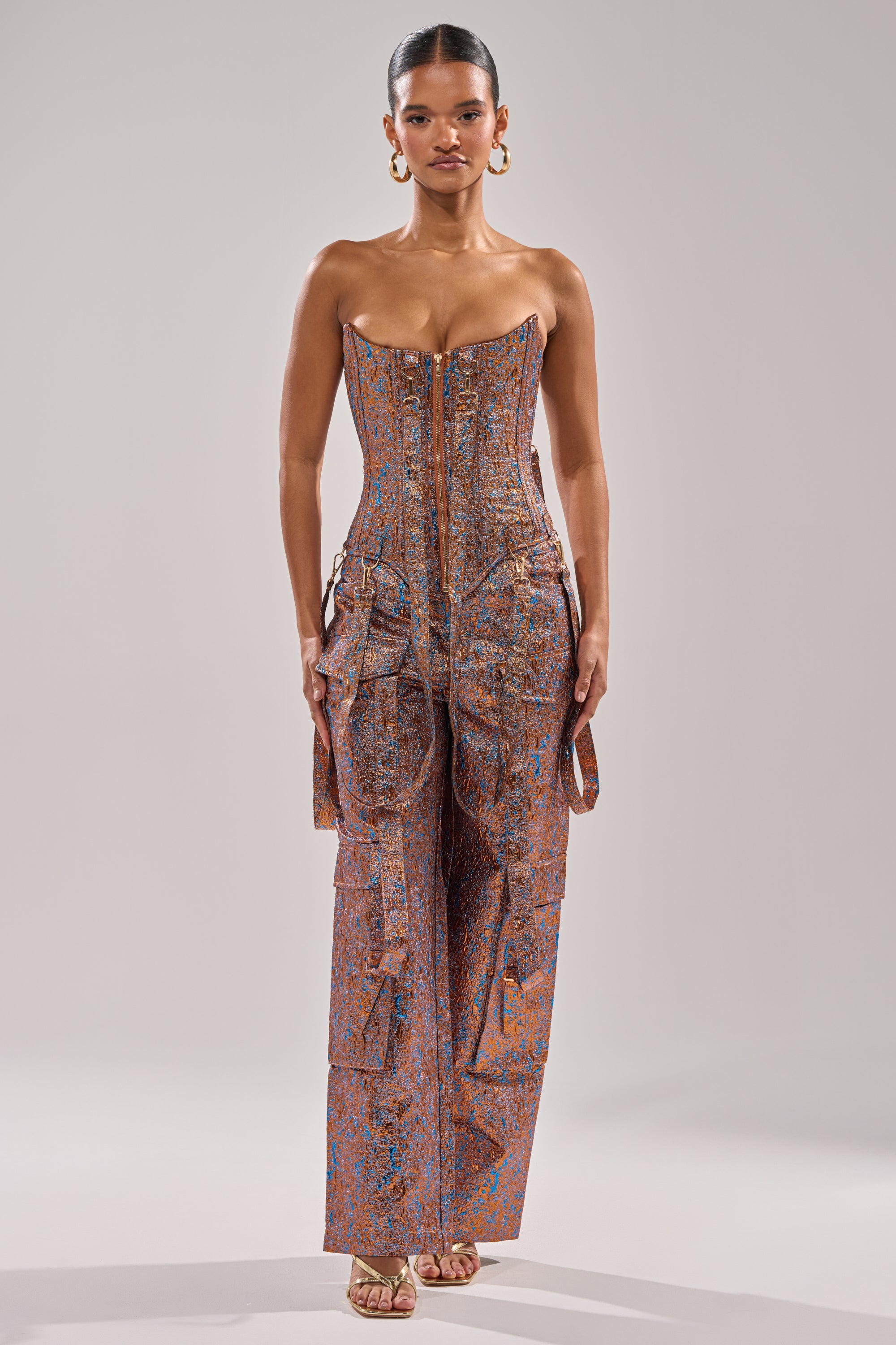 A woman exudes confidence in the CHECK IT OUT BROCADE BRONZE TROUSER, styled with gold hoop earrings, slicked-back hair, and gold open-toe heels. The chic look is set against a neutral background. 6