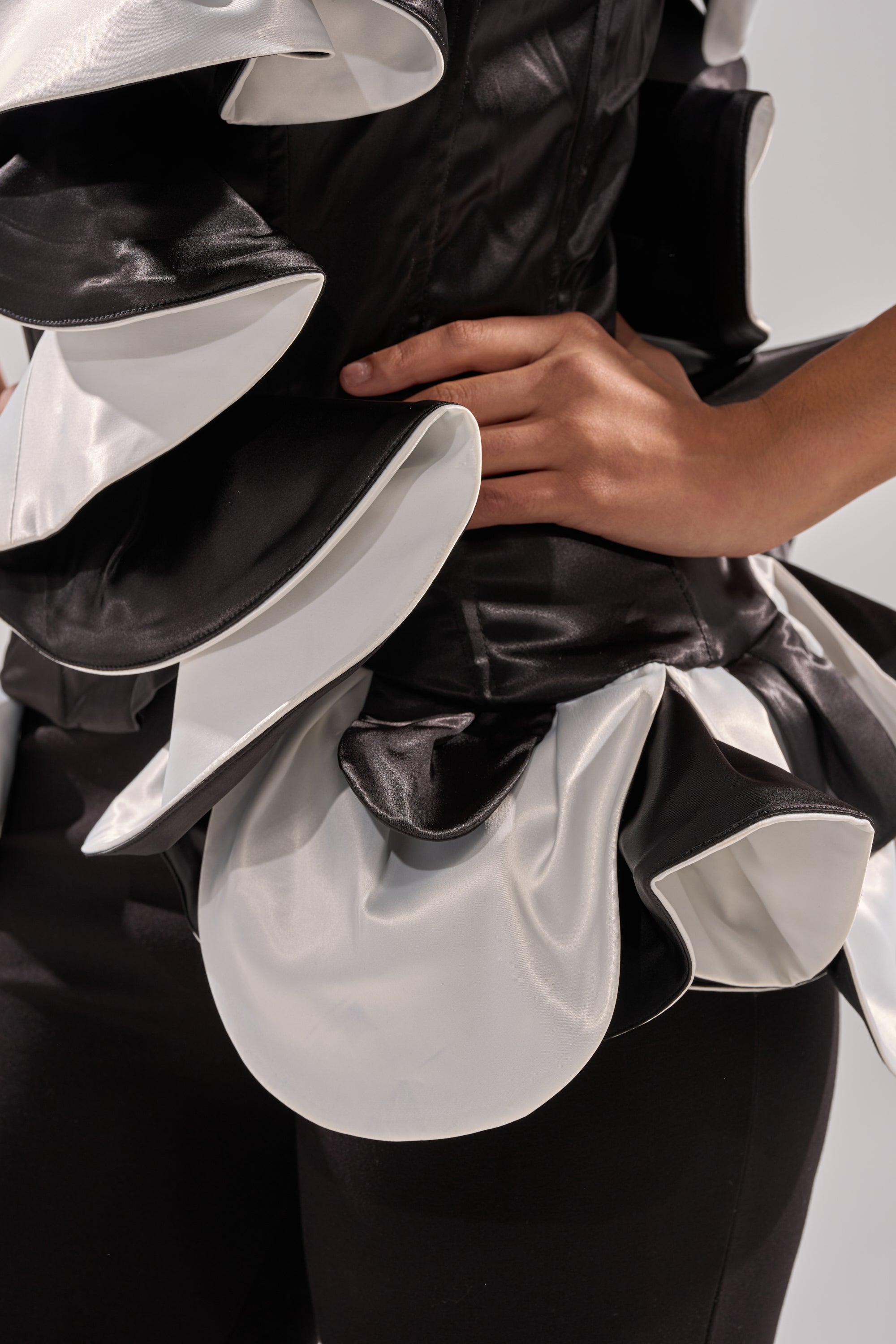 Wearing the SNOB IS A HABIT RUFFLE DETAIL SATIN TOP in black, a person poses with one hand on their waist, highlighting the couture-inspired ruffle details and textured satin layers.