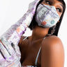 A stylish woman wears a sparkling face mask and matching CASH RULES RHINESTONE FASHION GLOVES adorned with sequins and colorful patches. She highlights her chic attire with dangling geometric earrings and a sleek bob hairstyle, posing with one hand resting gracefully against her head.