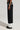 A person wearing the MIDNIGHT IN PARIS TROUSER, featuring black fabric with white cuffs and side pocket details, showcases a sleek high-rise waist. The non-stretch material beautifully enhances the look, elegantly paired with black shoes. A plain, light-colored background highlights the trouser's timeless appeal.