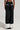 The image showcases the back view of a person wearing the MIDNIGHT IN PARIS TROUSER, featuring a black wide-leg silhouette with white cuffs and two white pocket accents. These high-rise waist pants are made from non-stretch fabric and are styled with black shoes against a plain, light-colored backdrop.