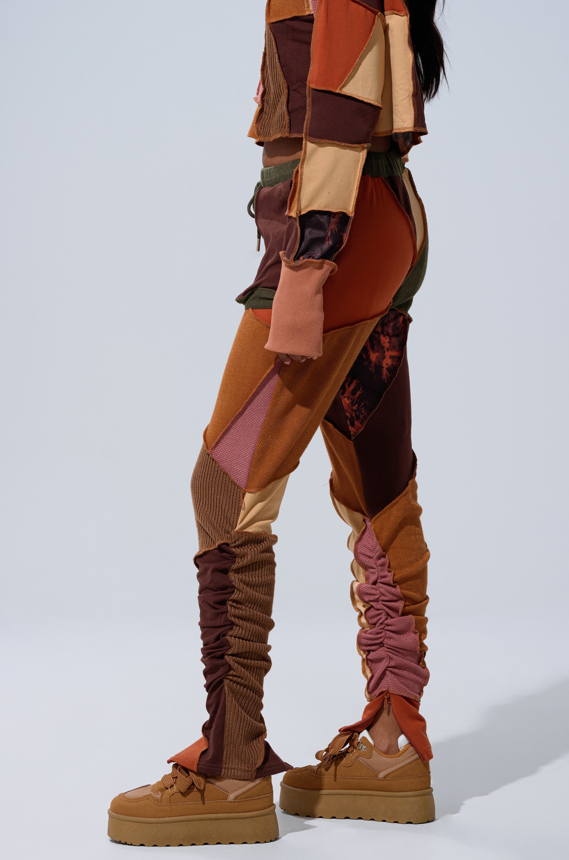 Someone wearing the CATCH FEELINGS PATCHWORK LEGGING and a matching top in brown, orange, and pink tones with tan platform sneakers. The outfit features mixed textured fabrics and ruched pant legs for added style.