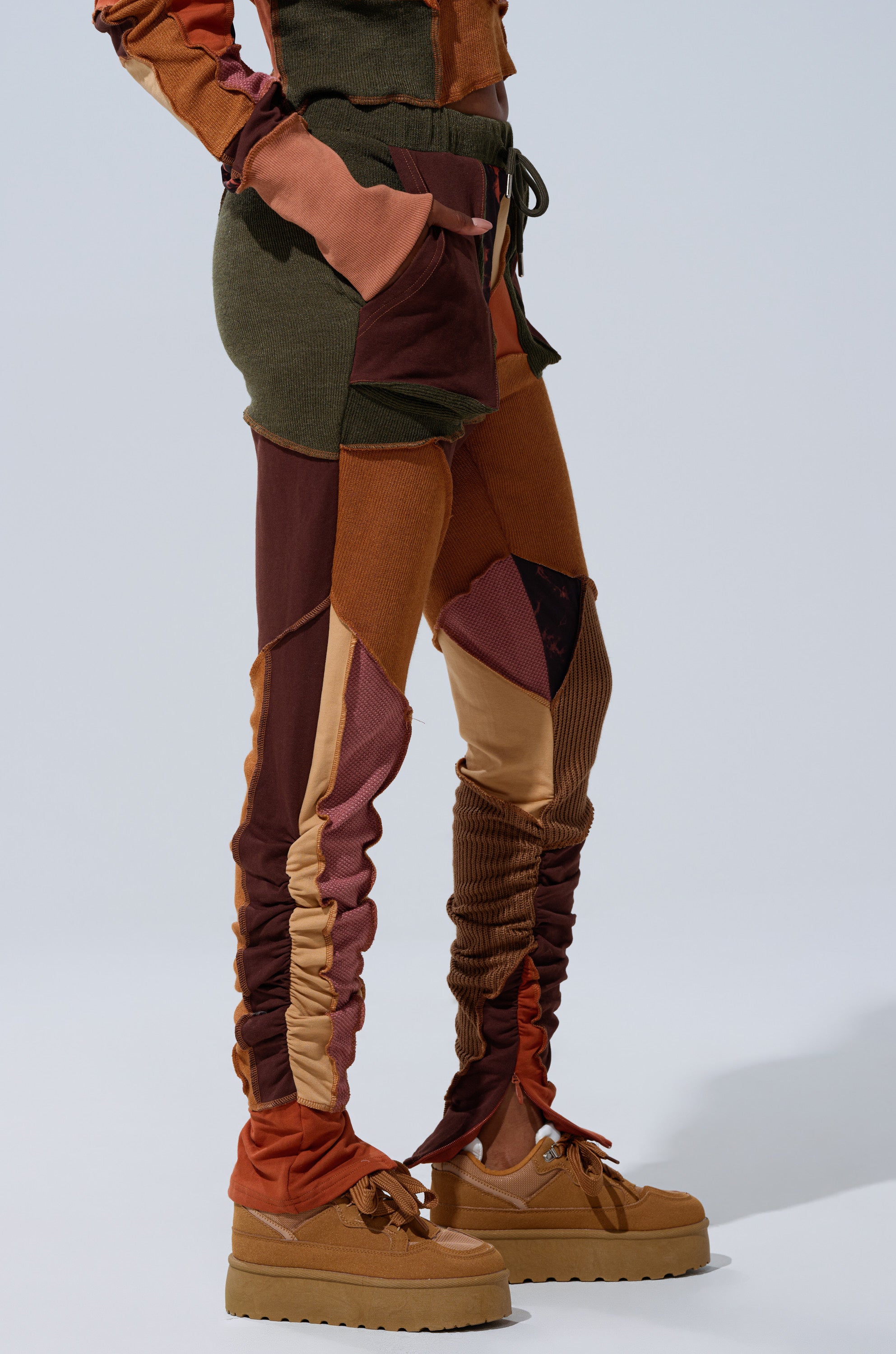 Wearing the CATCH FEELINGS PATCHWORK LEGGING in brown, orange, and burgundy with tan platform shoes, a person stands against a plain light background.