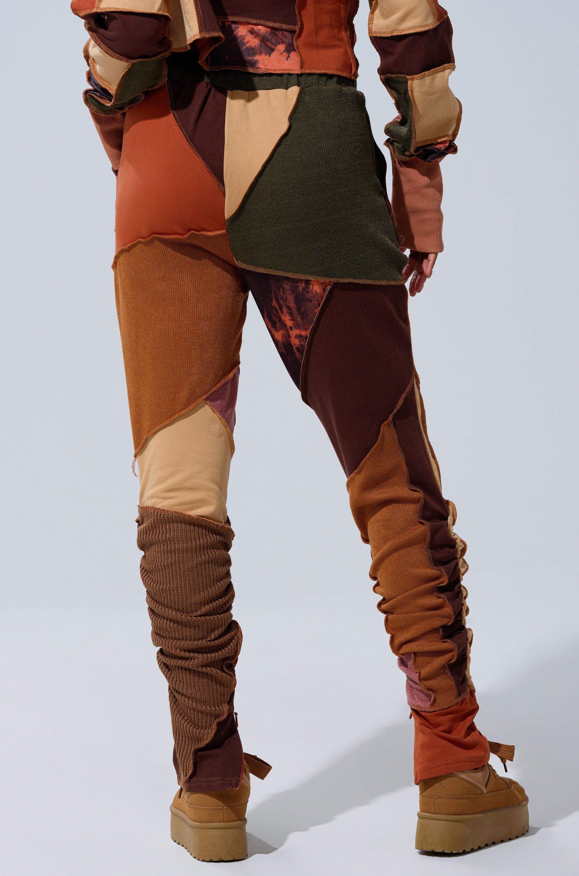 Wearing the CATCH FEELINGS PATCHWORK LEGGING in brown, orange, and beige with layered textures and gathered fabric, a person stands on a light background showing only their lower back and legs.