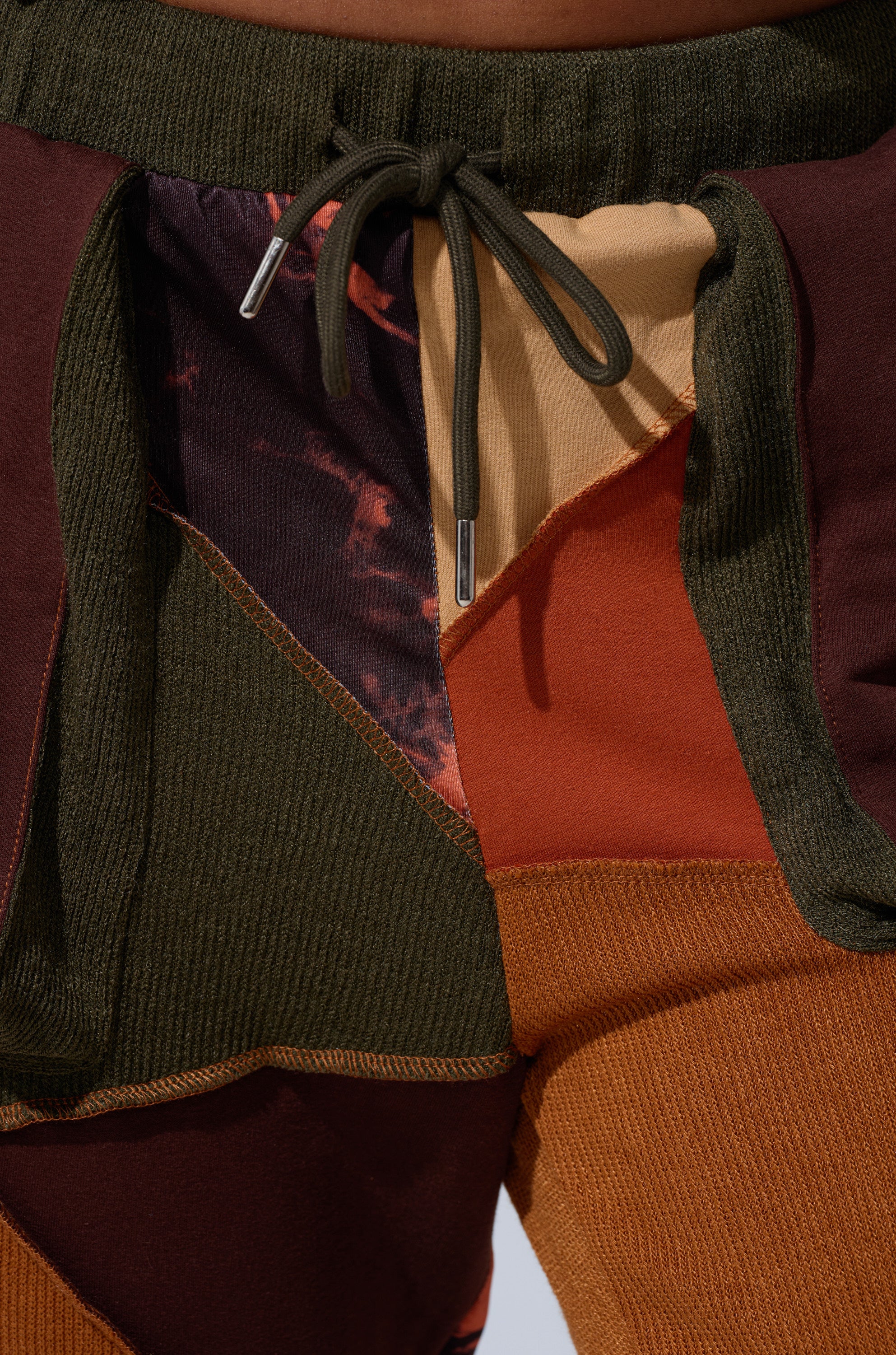 Close-up of CATCH FEELINGS PATCHWORK LEGGING with drawstring, elastic waist, and a color-block patchwork design in olive green, maroon, orange, tan, and patterned fabrics.