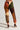 A person wearing CATCH FEELINGS PATCHWORK JOGGER pants, featuring a mix of brown, green, orange, beige, and purple colors, stands on a plain background. The stretchy cotton joggers are designed with varied textures and geometric patterns. They complete their look with dark high-heeled shoes.