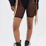 A person wears the BARELY THERE MESH BIKER SHORT in black with a high-rise elastic waist, paired with black underwear, lace-up combat boots, and a black jacket featuring colorful ribbon details against a light background.