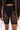 Wearing the BARELY THERE MESH BIKER SHORT with a high-rise elastic waist over opaque black underwear, styled with a black top and a jacket adorned with colorful ribbon accents on the sleeves.
