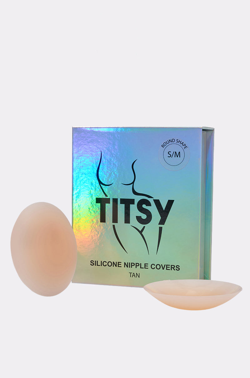Two tan silicone nipple covers are displayed beside a holographic box labeled "TITSY THIN EDGE SILICONE NIPPIE COVER, Tan," featuring an outline of a body and an "S/M" size sticker for discreet breast coverage.
