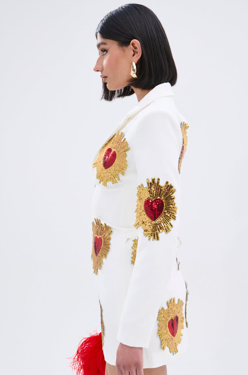 A woman with straight dark hair stands in profile against a plain white background, wearing the GLISTENING IN GOLD BLAZER DRESS IN WHITE.