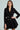 A woman confidently wears the HBIC BLAZER MINI DRESS, a chic black design with double-breasted gold buttons. Her long, straight hair cascades down as her neutral expression exudes poise against a soft, light background.