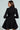 A woman wears the HBIC BLAZER MINI DRESS, a fitted black coat dress with long sleeves and a peplum hem, while looking to the side against a plain light background.