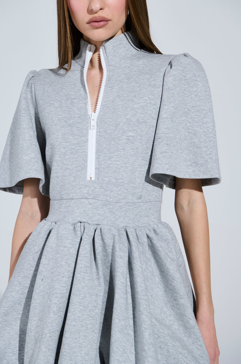 The NAME OF THE GAME SHORT SLEEVE ZIPPERED MINI DRESS in light gray showcases comfortable chic style with its high collar, wide short sleeves, and zip front. The flared skirt complements its plain backdrop, making it a versatile wardrobe essential.