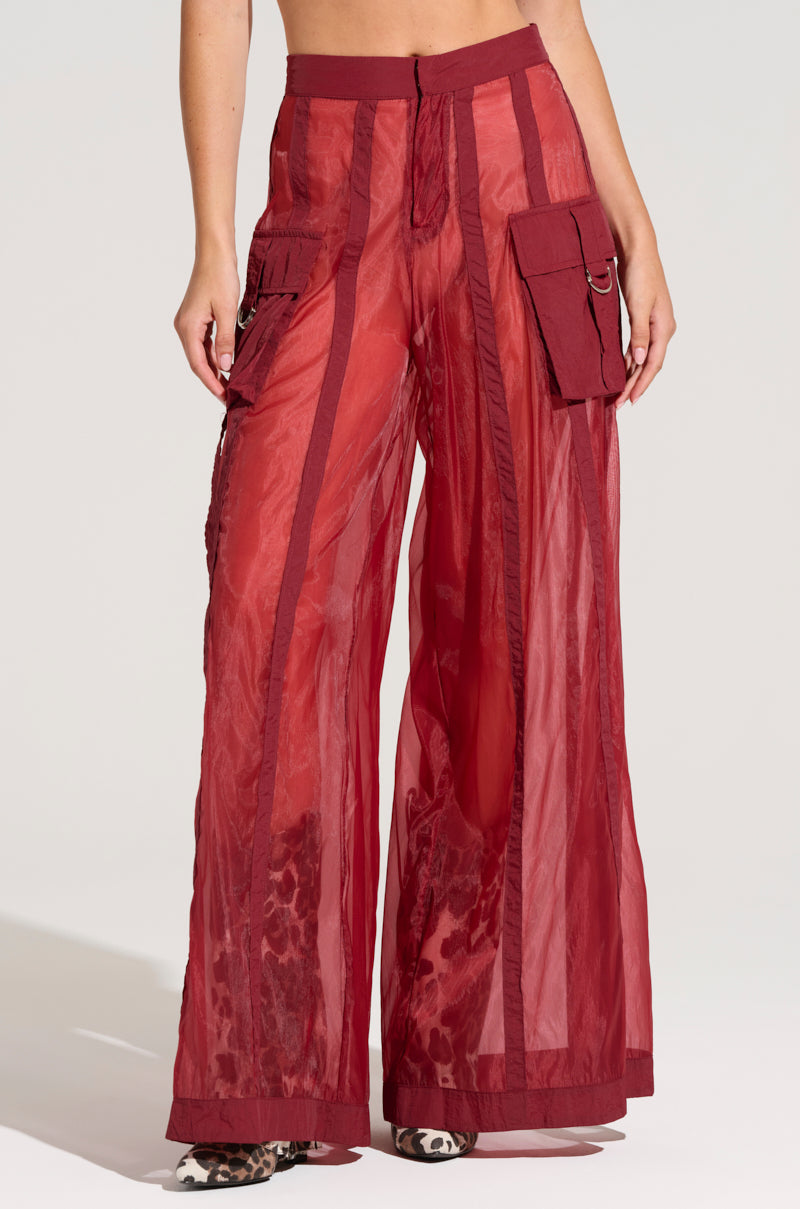 A person modeling the CELINE WIDE LEG TROUSER, which are sheer, high-rise, wide-leg burgundy pants featuring solid side stripes, cargo-style pockets on each thigh, and leopard-print shorts visible underneath. The person is standing against a plain background with only the lower torso and legs visible.