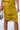 Close-up of a person wearing the ASH Strapless Cargo Maxi Dress in mustard yellow. They are holding a silver chainmail handbag in their left hand. The ruched side detailing runs vertically down the left side of the dress, creating gathered folds.