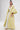 A woman wears the VENICE BROCADE PUFF SLEEVE DUSTER, a long yellow and light blue floral kimono with layered sleeves, over a white lace crop top and white pants, radiating vintage charm against a plain white background.