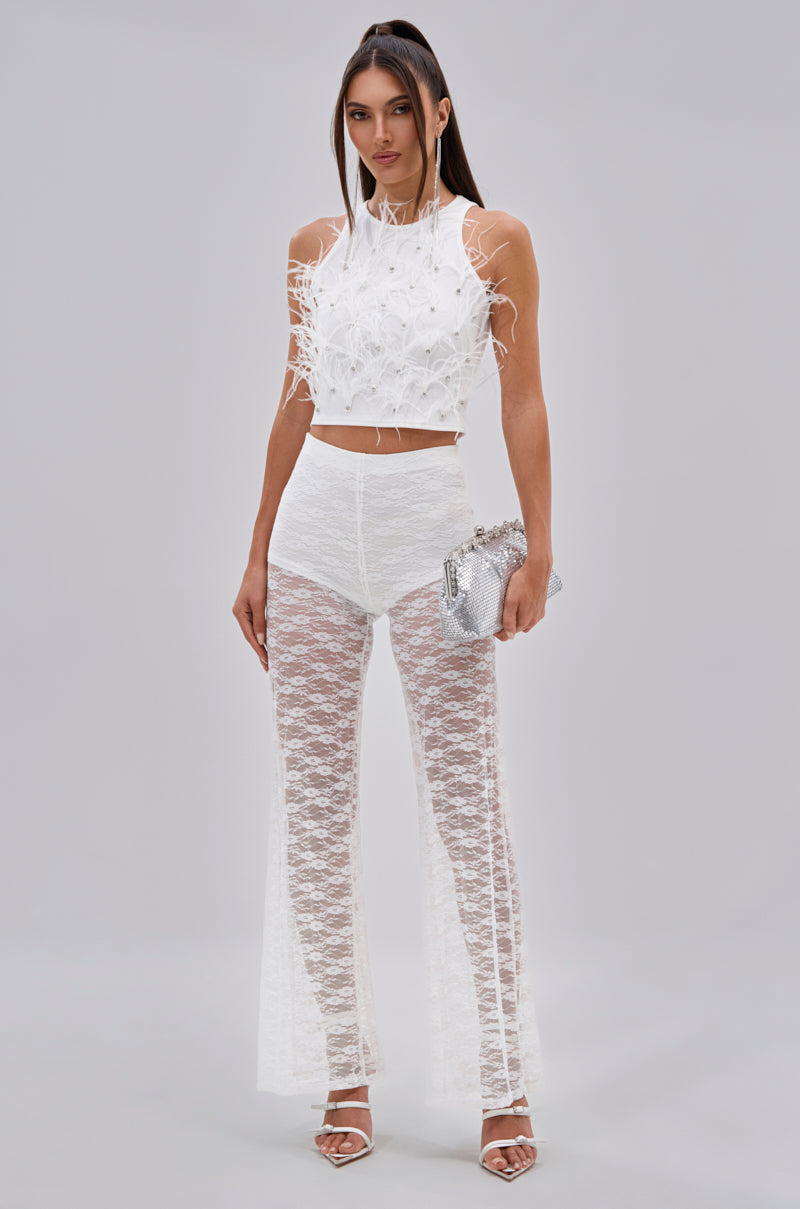 Against a light gray background, a woman wears the BIRDS OF A FEATHER SLEEVELESS TOP with sheer white lace pants over high-waisted briefs, carries a silver purse, and finishes the look with white high-heeled sandals. 5