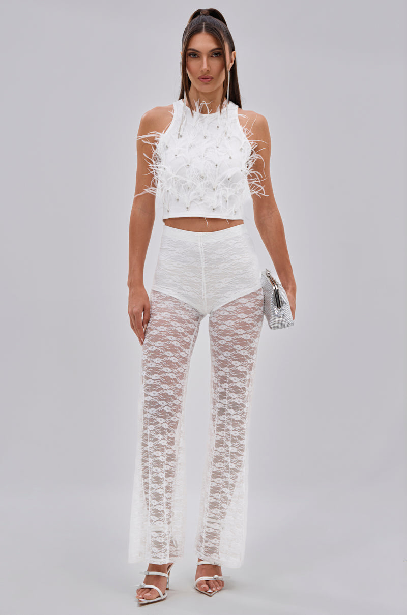 A woman faces forward wearing the BIRDS OF A FEATHER SLEEVELESS TOP with high-waisted sheer lace pants over white briefs, holding a silver clutch and wearing white heels. Her hair is straight and her expression neutral. 6