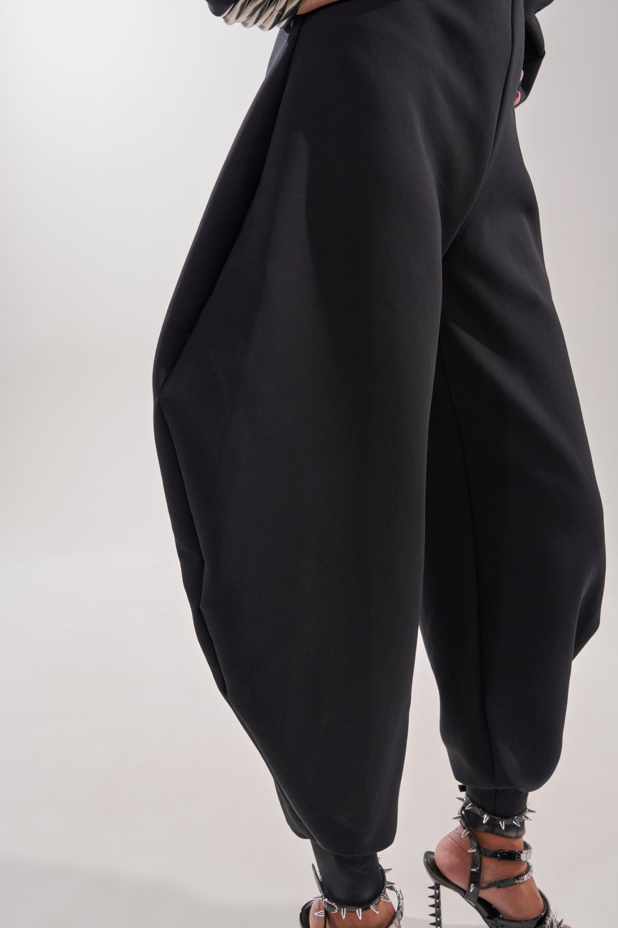 A person wearing the COMFY COZY SWEATSHIRT JUMPSUIT IN BLACK with wide legs and black ankle-strap high-heeled sandals stands against a plain light background. 10