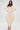 A woman models the COMFY COZY SWEATSHIRT JUMPSUIT IN BONE against a white backdrop. The stretchy, sculpted design with fitted ankles is perfect for lounging, styled here with straight hair, gold jewelry, and open-toe heels.