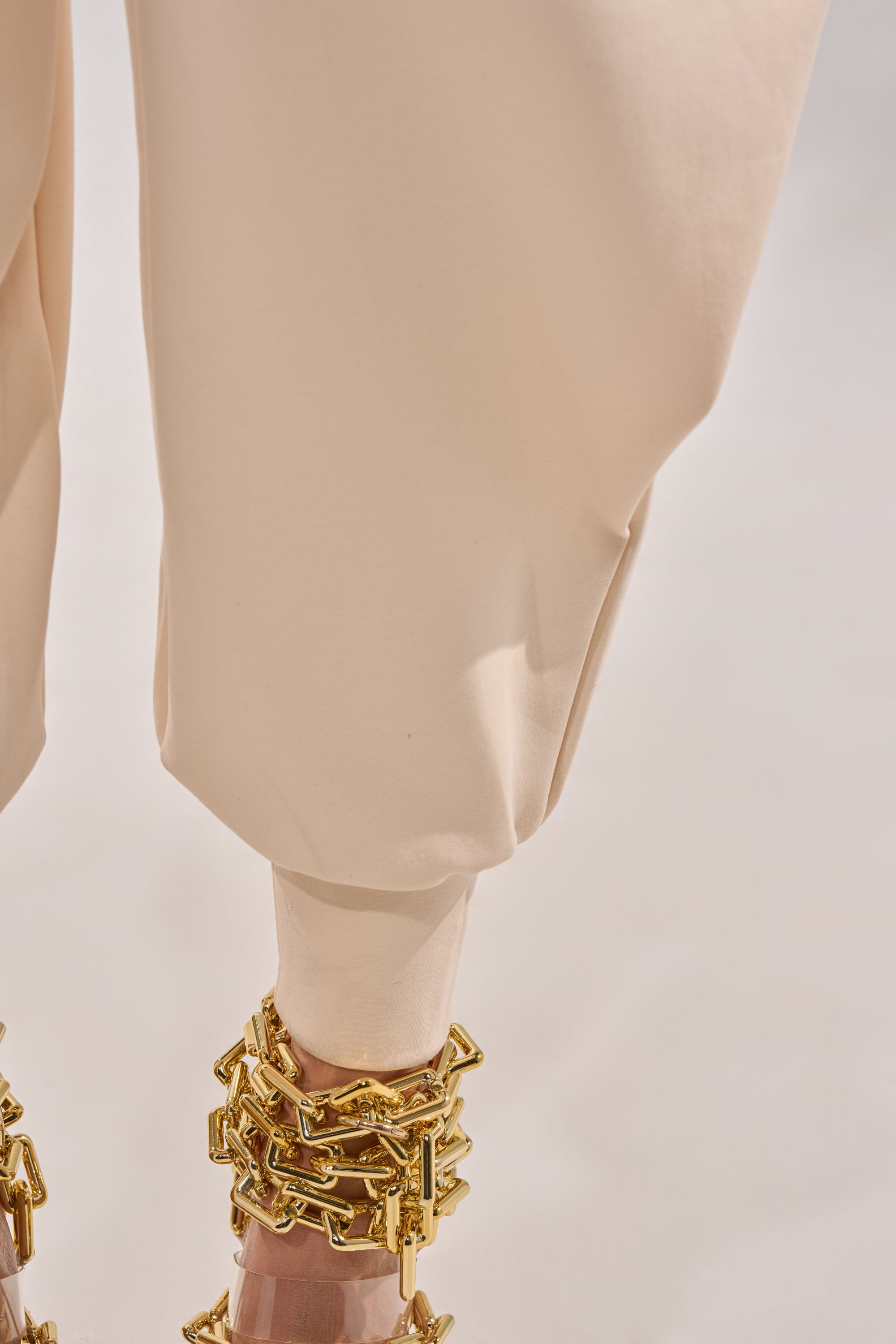 A close-up of a person wearing the COMFY COZY SWEATSHIRT JUMPSUIT IN BONE with gold chain anklets, standing on a light-colored surface. 7