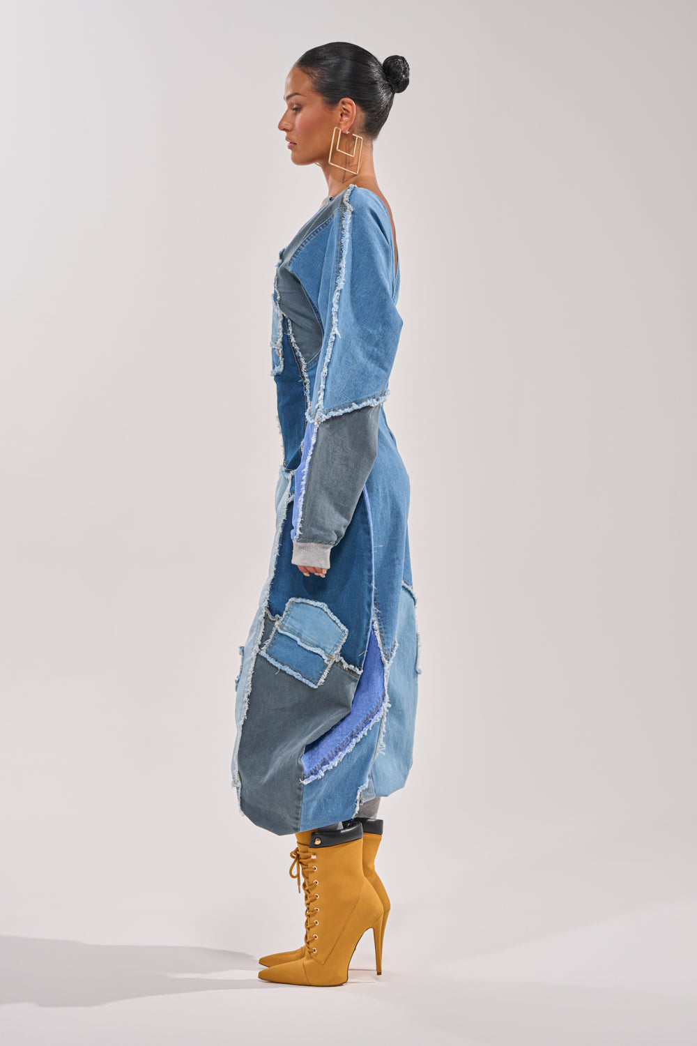 A woman in profile wears the COMFY COZY JUMPSUIT IN DENIM PATCHWORK with yellow lace-up high-heeled boots, a neat bun, and large square earrings. She stands against a plain white background. 4