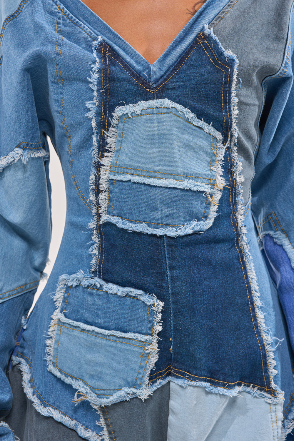 Close-up of the COMFY COZY JUMPSUIT IN DENIM PATCHWORK, showcasing frayed blue denim patches, visible stitching, and a V-neckline for a modern streetwear-inspired distressed look. 6