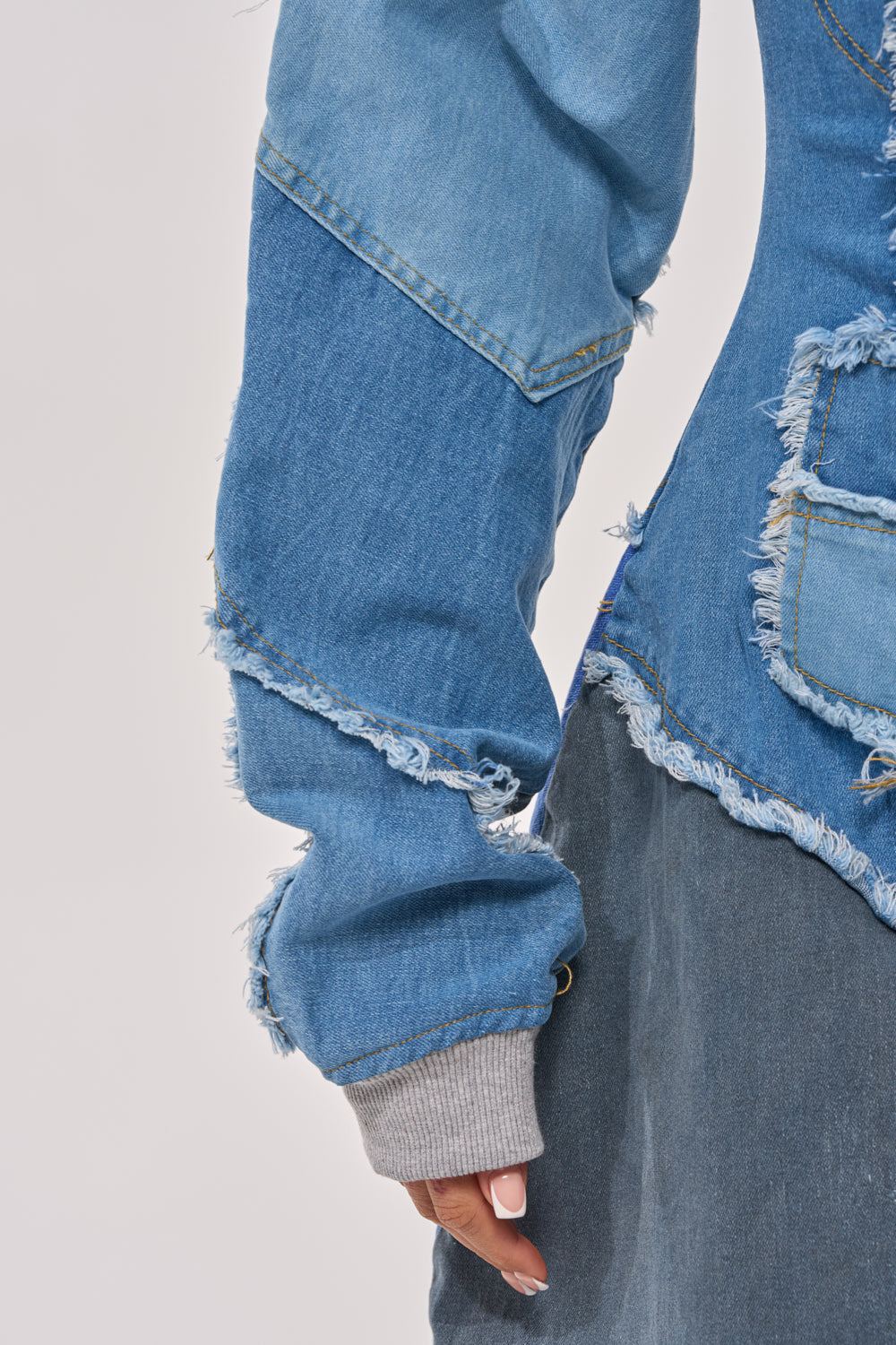 A close-up of a person wearing the COMFY COZY JUMPSUIT IN DENIM PATCHWORK, with frayed edges and a streetwear vibe, layered over a gray skirt and gray sweater cuffs peeking from the jacket-style sleeves. 7