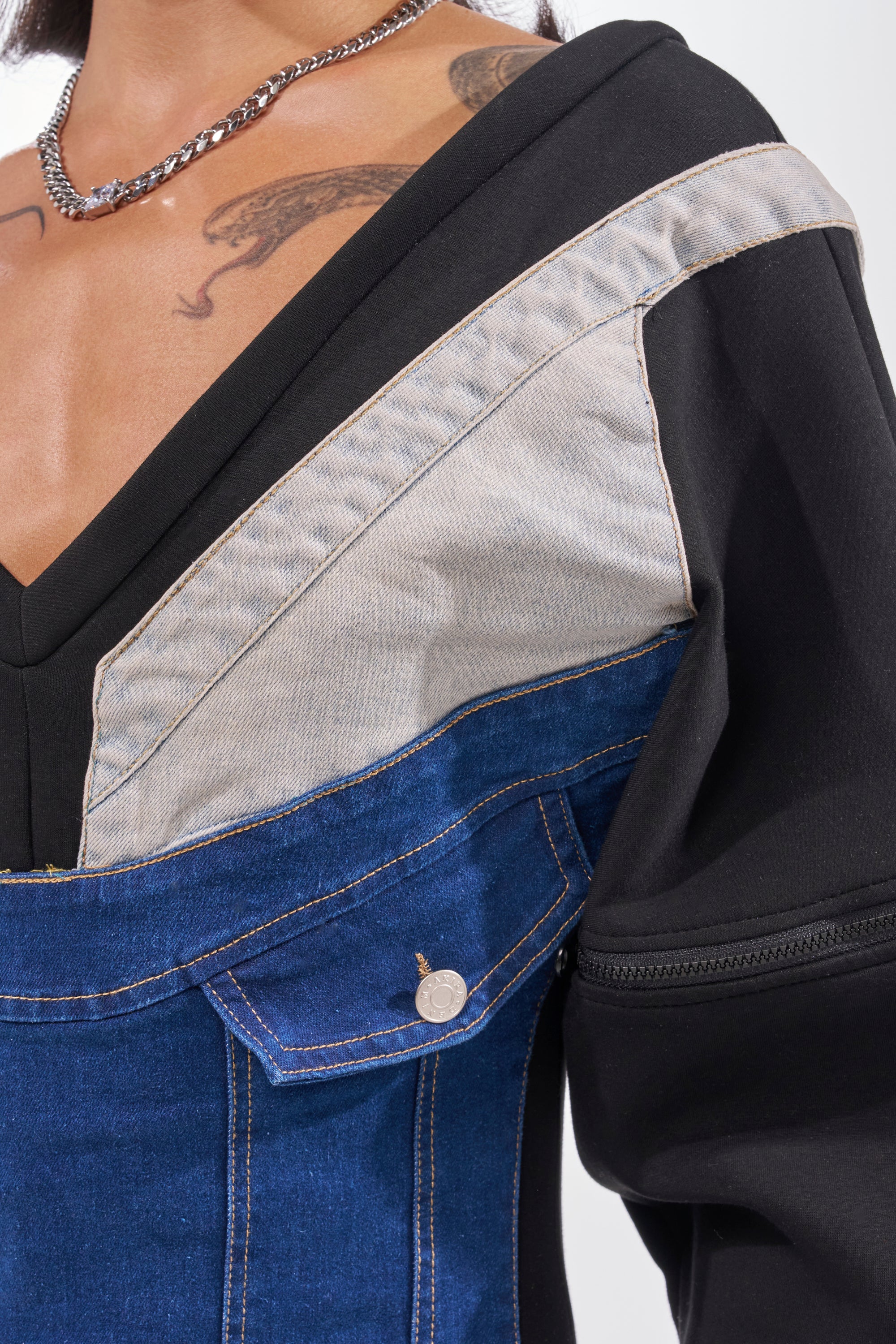 A person sports the COMFY COZY SWEATSHIRT JUMPSUIT IN PATCHWORK DENIM IN BLACK, showcasing diagonal color-block denim accents and visible stitching, styled with a chain necklace and chest and shoulder tattoos for a bold streetwear vibe. 7