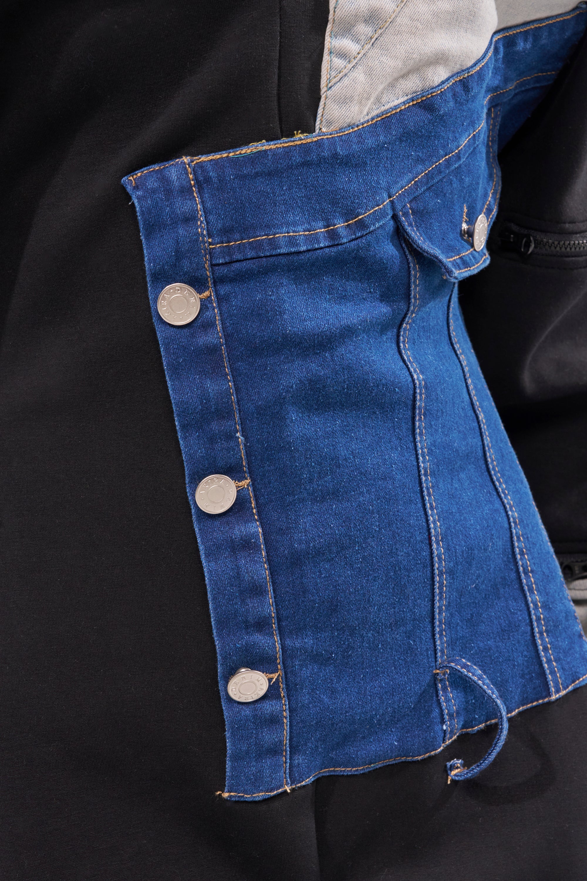 Close-up of the COMFY COZY SWEATSHIRT JUMPSUIT IN PATCHWORK DENIM IN BLACK, featuring silver buttons and visible stitching, draped over a black fabric surface. 8
