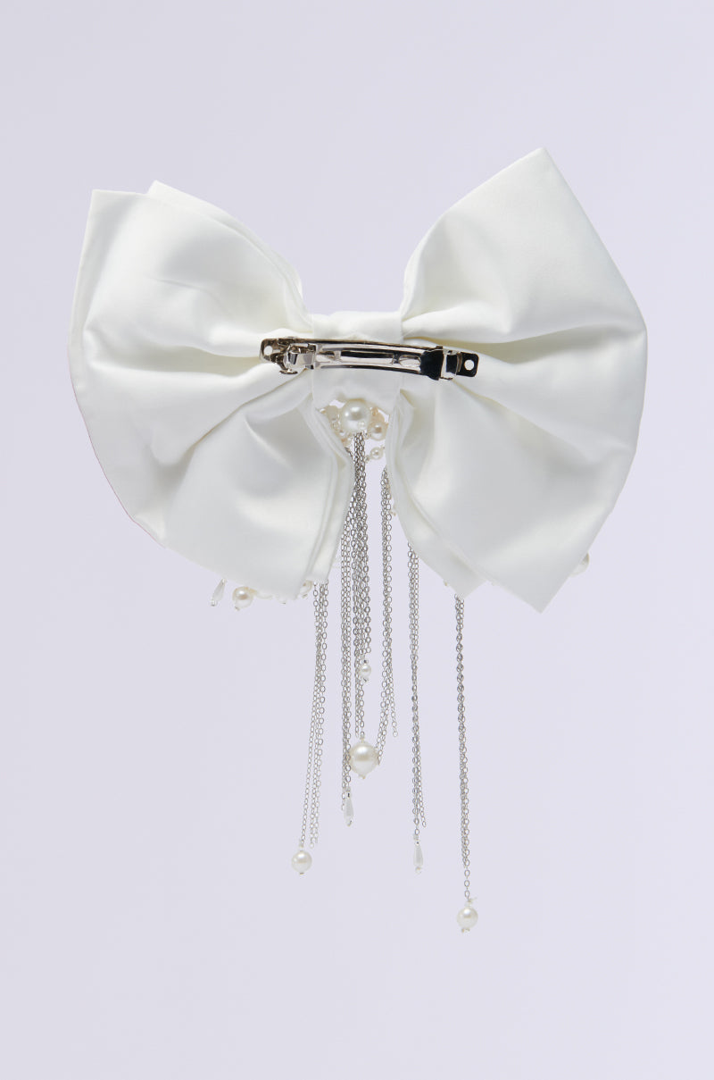 The WINTER WHITE BLING HAIR BOW, a generously sized accessory crafted from satin fabric and embellished with dangling silver chains and pearl beads, is photographed against a plain light background. 2