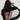 A woman showcases the ARI TULLE RUFFLE HIGH LOW DRESS IN BLACK, featuring a flowing silhouette with tulle ruffles and an eye-catching hemline. The dress includes a high neckline and short hem that gracefully extends into a long train. She stands on a plain background, exuding poise and confidence.